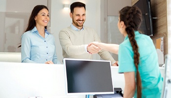 A couple shaking hands with a dental office team member