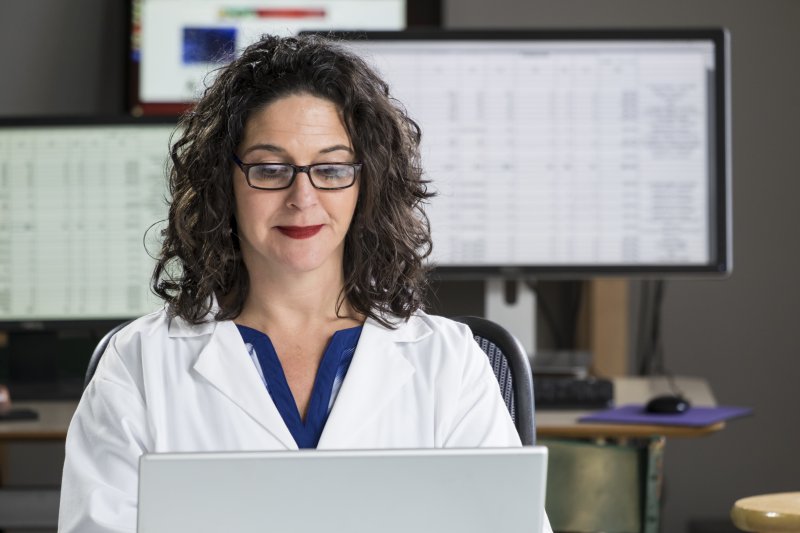 A middle-aged woman wearing a white medical coat sitting behind a computer