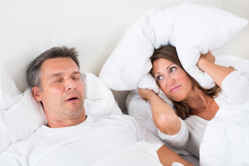 A woman with a pillow over her ears while her husband snores
