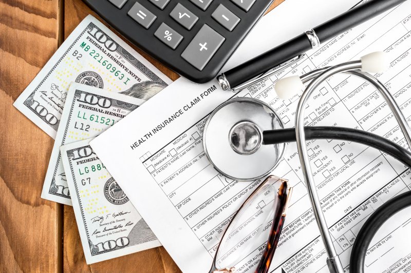 A calculator, stethoscope, money, a pen, and a health insurance claim form lying on a desk