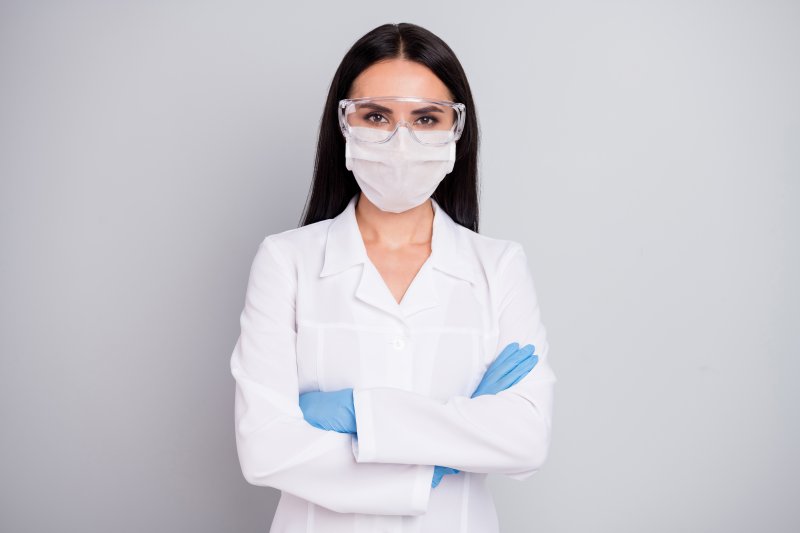 A female dentist wearing personal protective equipment and standing with her arms crossed