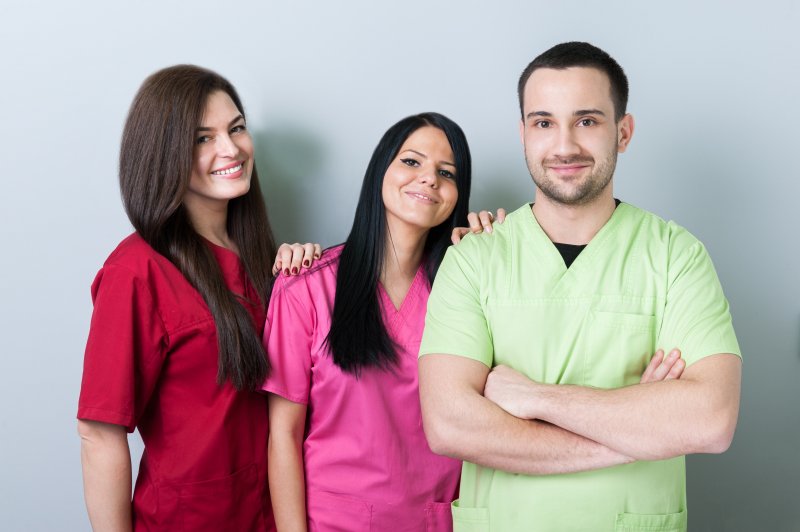 Three dental professionals standing next to each other and smiling, all wearing different colored scrubs