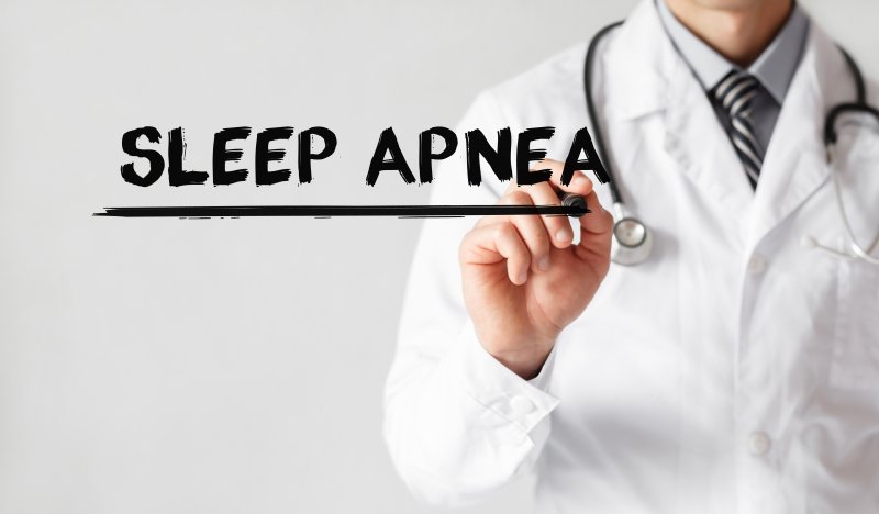 A doctor wearing a lab coat and stethoscope writing the words “Sleep Apnea”