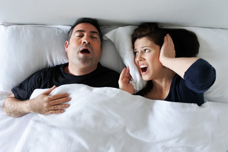 a man and woman lying in bed while he snores and she covers her ears 