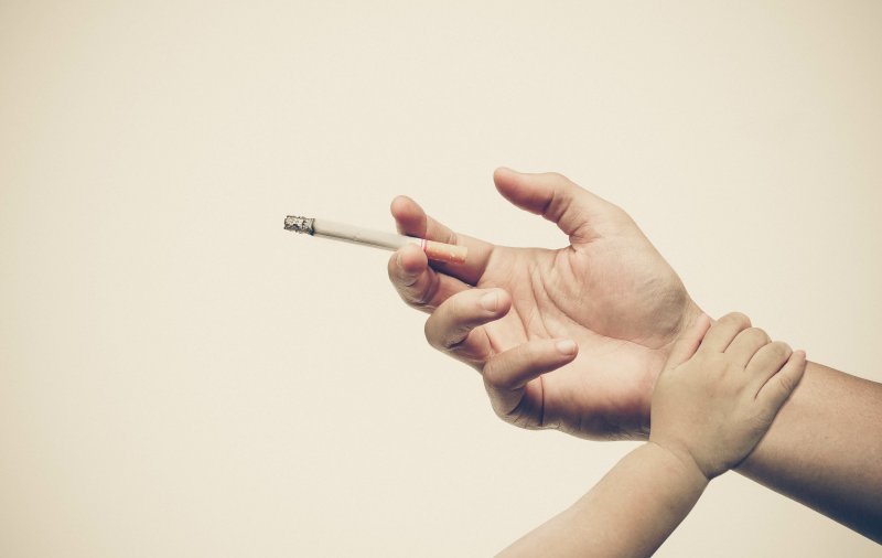 an image of an adult hand holding a cigarette and a child’s hand on their wrist